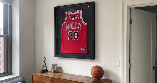 Maillot de basket rouge style Chicago Bulls numéro 23 encadré dans une vitrine murale noire, au-dessus d’un meuble en bois avec un ballon et un trophée.