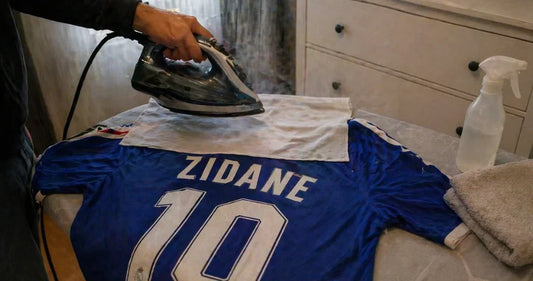 Personne essayant un maillot de football devant miroir avec plusieurs tailles S M L XL posées sur lit et mètre ruban pour choisir la bonne taille