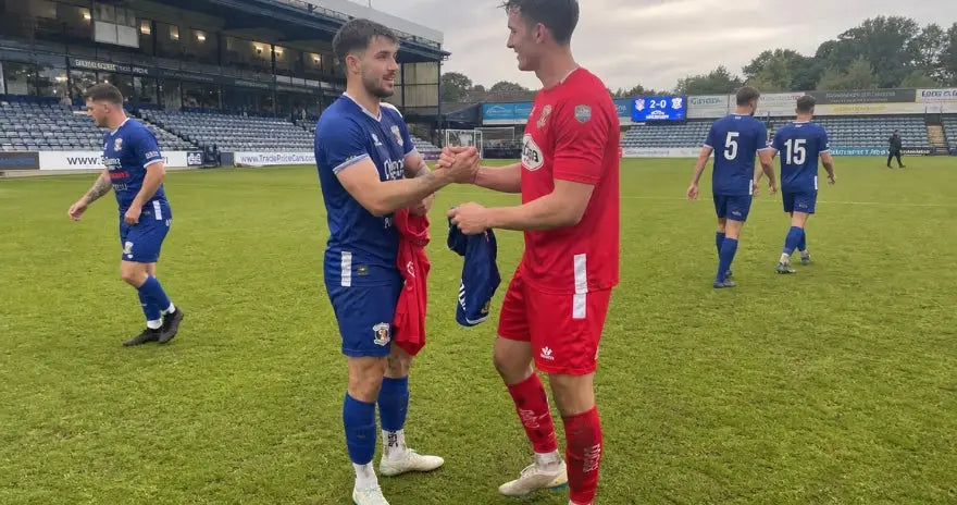 Deux joueurs de football se serrent la main sur le terrain après le match en commençant à échanger leurs maillots.