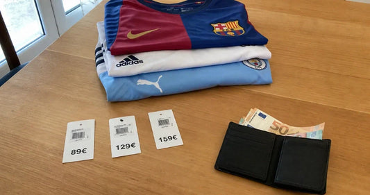 Trois maillots de football pliés sur une table en bois avec des étiquettes de prix et un portefeuille ouvert contenant des billets en euros.