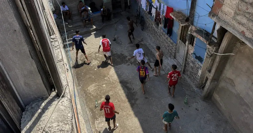 Photo aérienne réaliste d’un match de football improvisé dans une rue de favela au Brésil, avec des jeunes portant des maillots de clubs célèbres.